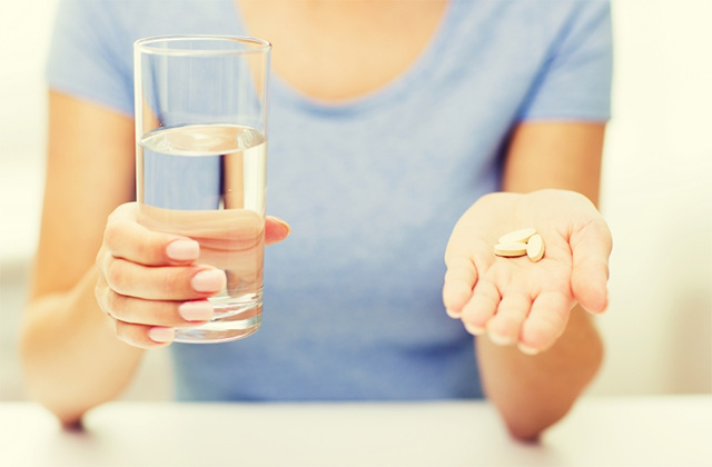 한 여성이 한 손으로는 물잔을 들고 있고, 한 손에는 알약이 놓여져 있다