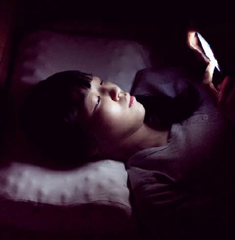 여자가 잠자리에 누워 스마트폰을 사용하고 있다.