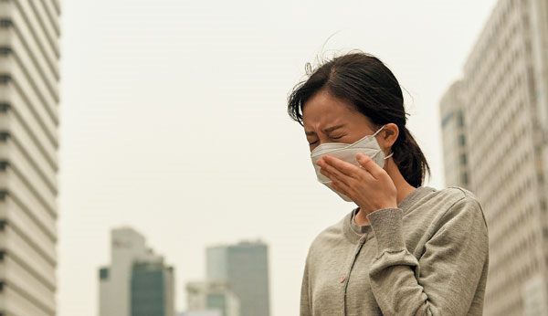 한 여성이 미세 먼지로 뿌연 도심에서 마스크를 하고 있다.