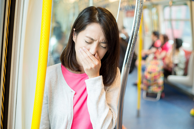 한 여성이 대중교통 안에서 메스꺼워하고 있다.