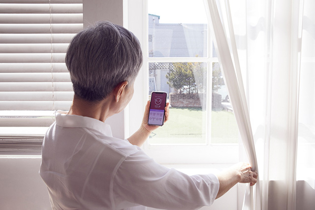 창문 앞에서 미세 먼지 농도를 휴대전화로 확인하는 여성 노인